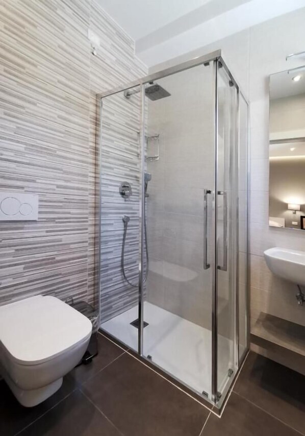 A modern bathroom with a glass-enclosed shower, a white toilet, and a sink with a mirror.
