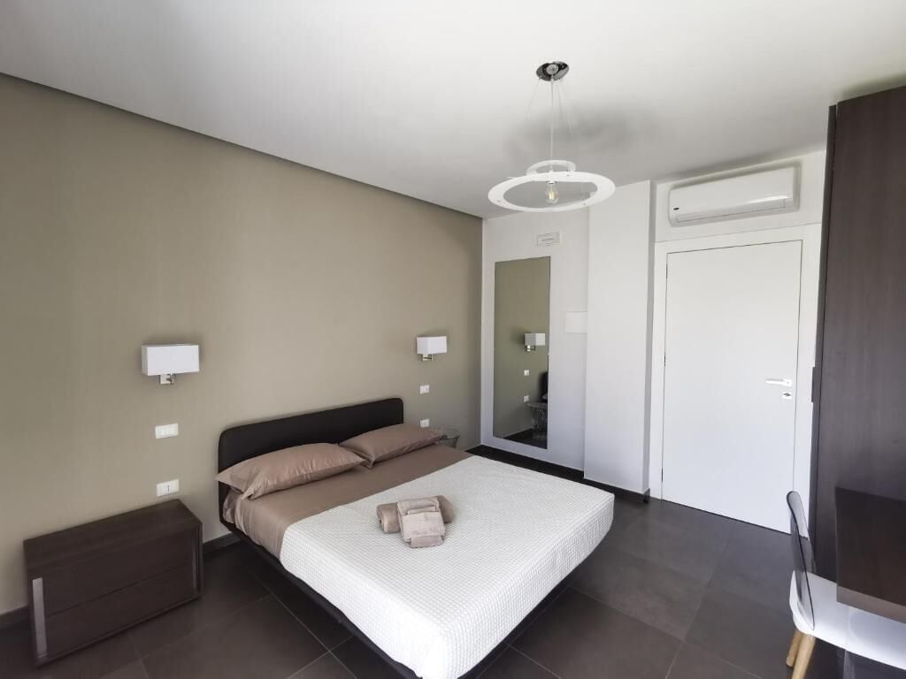 A modern bedroom with a bed, bedside lamps, a mirror, and a wardrobe.