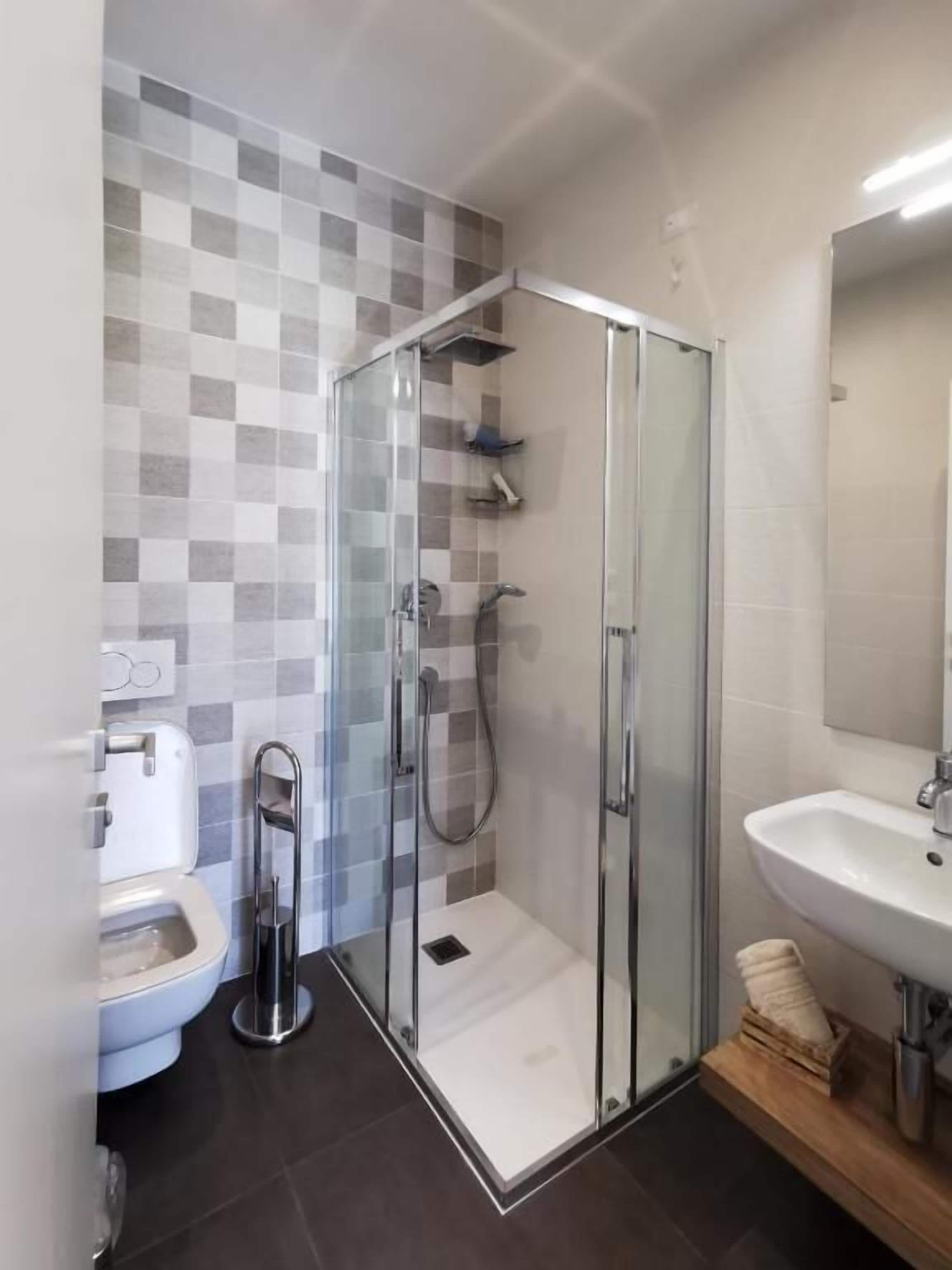 Een moderne badkamer met een douchecabine van glas, een witte wastafel en een toilet.