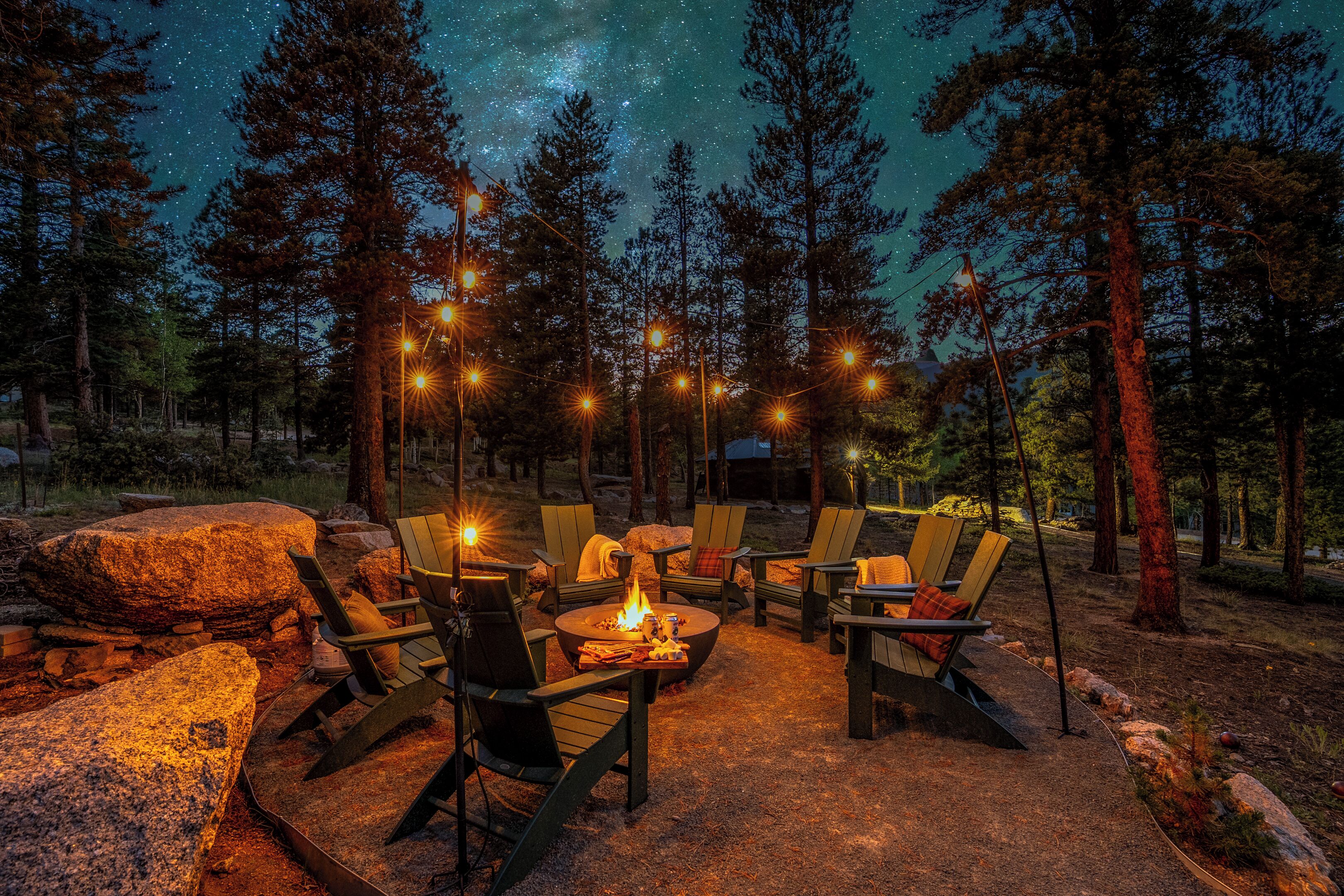 An outdoor seating area with chairs and a fire pit, surrounded by trees and a starry night sky.