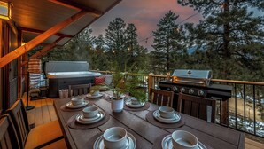 A wooden deck with a dining table set for four, surrounded by chairs.