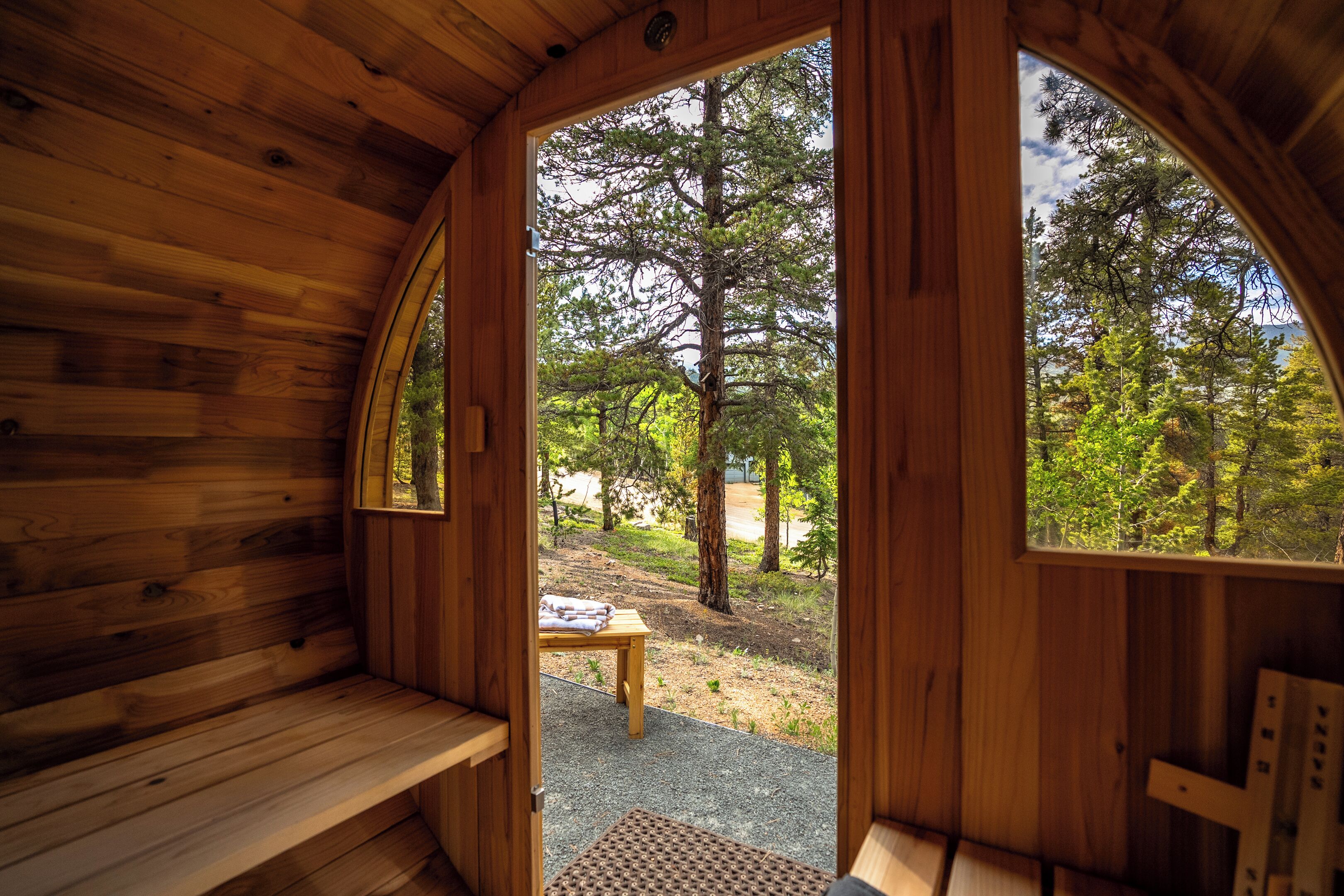 A wooden cabin with a bench and a table outside, surrounded by trees.