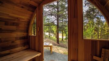 A wooden cabin with a bench and a table outside, surrounded by trees.