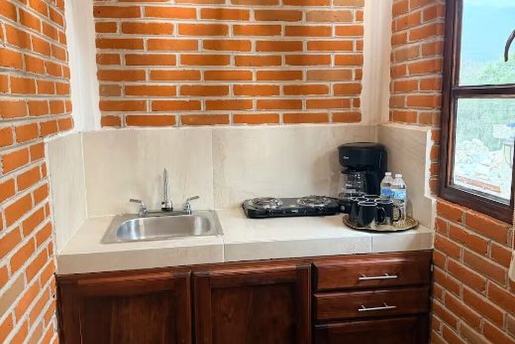 A compact kitchen with a brick wall, a sink, a coffee maker, and a window.