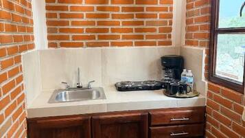 A compact kitchen with a brick wall, a sink, a coffee maker, and a window.