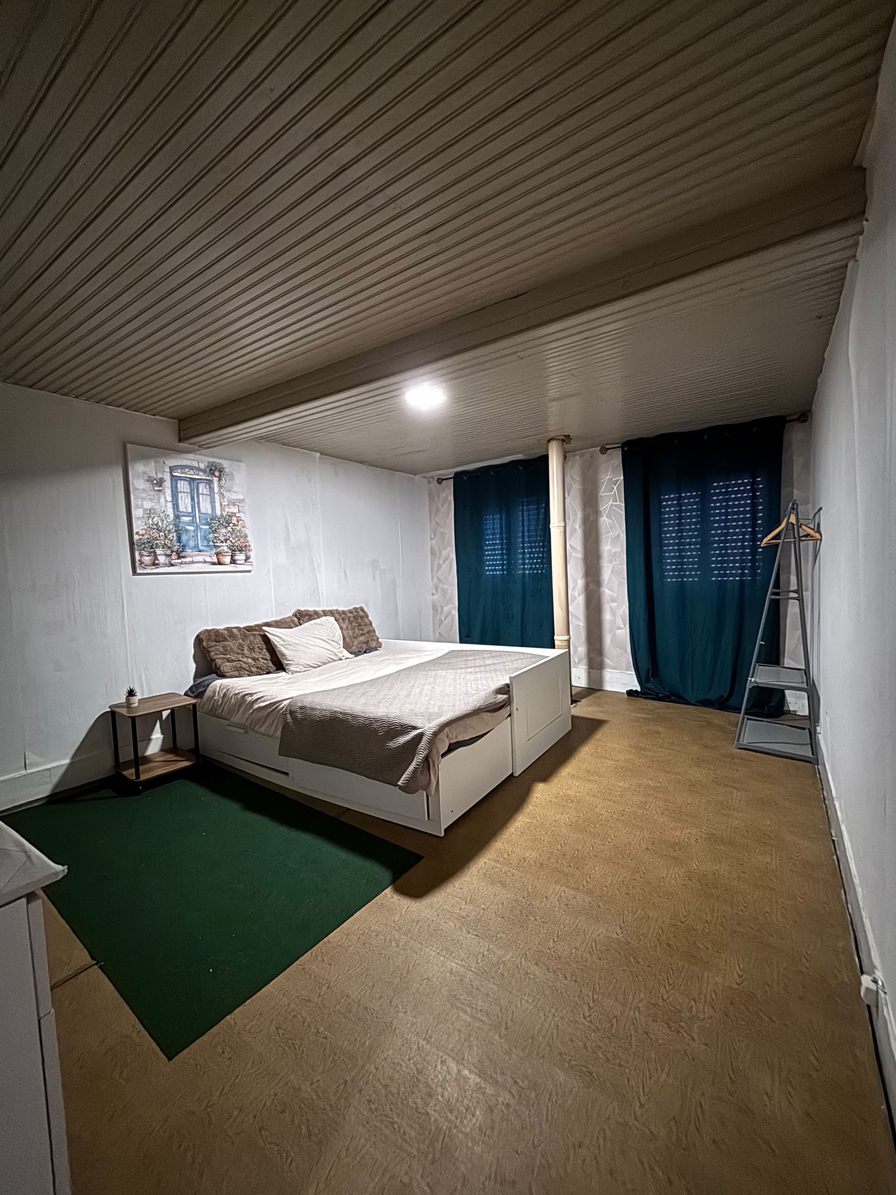 A bedroom with a bed, a nightstand, a ladder, and a painting on the wall.