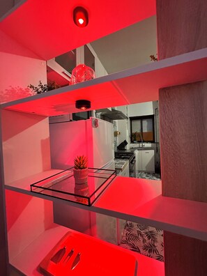 Una cucina moderna con uno scaffale illuminato di rosso, un tavolo con piano in vetro e una pianta in vaso.
