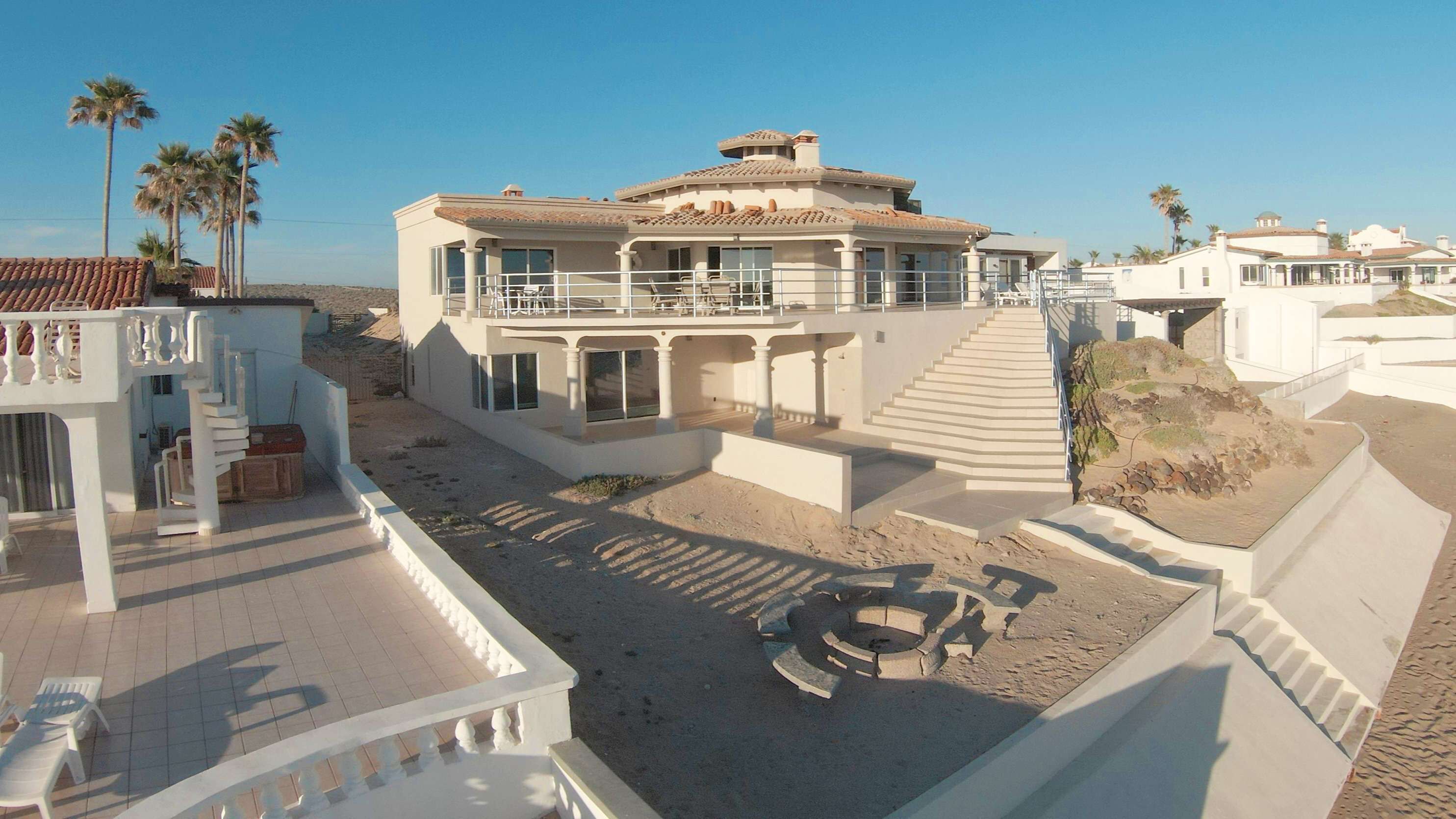 Une propriété située sur la côte, comprenant une grande maison, un patio et un escalier menant à l’étage supérieur.