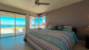 A bedroom with a large bed, a ceiling fan, and a view of the beach through a sliding glass door. - The Beach House | 3BR Beachfront Home | Sleeps 10 (Puerto Peñasco)