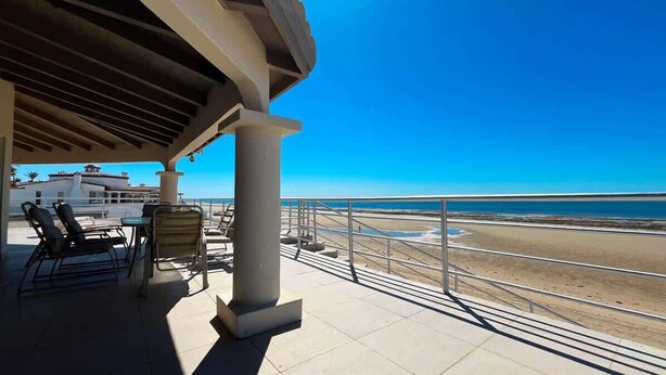 A covered outdoor area with a view of the beach, a table with chairs, and a railing. - Spacious Family Beachfront Home The Beach House (Puerto Peñasco)