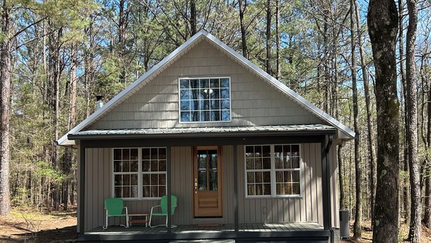 Une petite cabane avec un porche à l’avant, une seule porte et une fenêtre.