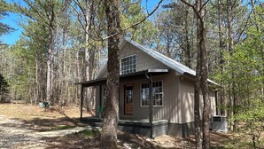 Une cabane avec une véranda, une petite terrasse et une fenêtre donnant sur la forêt.