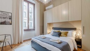 Quarto moderno com cama grande, radiador, janela com cortinas e ar condicionado fixado na parede.