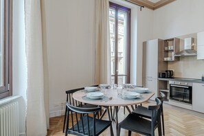 A dining area with a round table set for four, a kitchen with modern appliances, and a window with a view of buildings. - Quaint 2-bedroom apartment with AC in charming Torino (Torino)