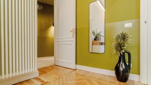 Um corredor com radiador, porta branca, espelho e planta em vaso.