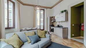 Um apartamento moderno com sofá cinzento, cozinha, área de refeições e vista para o edifício.