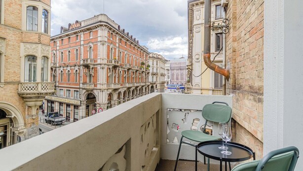 Uma varanda com mesa e cadeiras, com vista para uma rua com edifícios históricos.