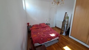 Una camera da letto con un letto, pavimento in legno, un lampadario, un termosifone e un armadio.