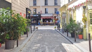 Una strada acciottolata fiancheggiata da edifici, un caffè con tavolini all'aperto e un cartello con su scritto 'Paris Coach'.