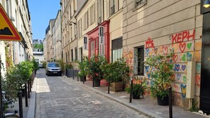 Una strada acciottolata fiancheggiata da edifici, alcuni con insegne e graffiti.