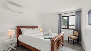 Ein Schlafzimmer mit einem Holzbett, Nachttischen, einem Sessel, einem Fenster mit Vorhängen und einem Bild an der Wand.