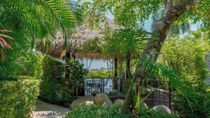 A lush garden with a pathway, a thatched-roof structure, and a view of the sea. - Oceanview Condo with Private Pool in Los Sueños (Herradura)