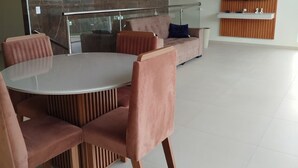 A modern living room with a round glass-top table, cushioned chairs, a sofa, and a mounted TV.