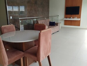 Una sala de estar moderna con una mesa redonda de vidrio, sillas acolchadas, un sofá y un televisor montado.