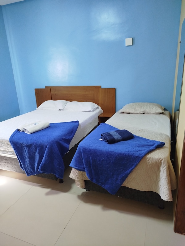 Dos camas individuales con cabeceros de madera, ropa de cama blanca y beige, y toallas azules.