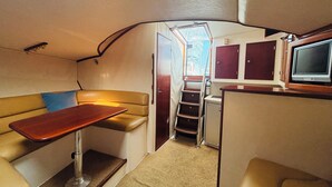 A compact interior with a sofa, a small table, a TV, and a staircase leading to an upper deck.