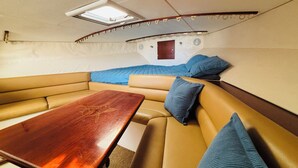 A boat interior with a wooden table, cushioned seating, a skylight, and a small door.