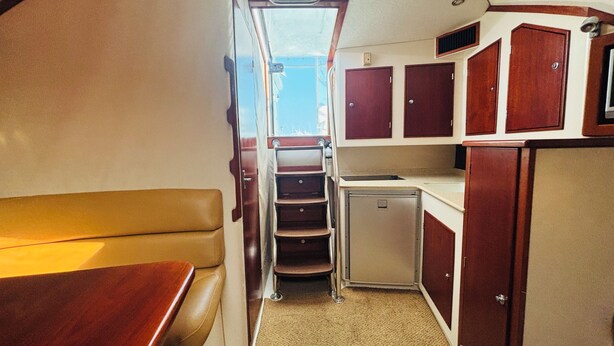 A compact kitchen with wooden cabinets, a small refrigerator, and a bench seating area.