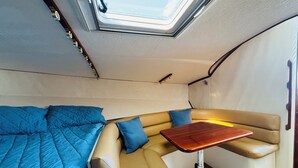 A compact interior with a bed, a seating area with cushions, a small table, and a skylight.