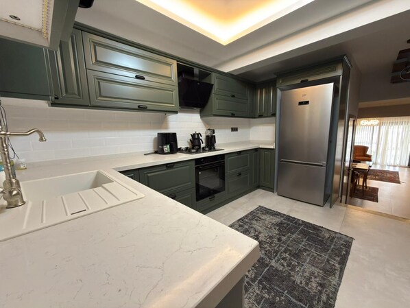 A modern kitchen with green cabinets, a white countertop, a built-in oven, and a refrigerator.