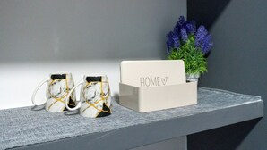 A shelf with two ceramic mugs, a white box with 'HOME' and a heart symbol, and a potted plant with purple flowers. - Deluxe Double Room 101 (Catania)
