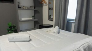 A neatly made bed with white linens and rolled towels, a small bedside table, a mirror, and a potted plant. - Deluxe Double Room 101 (Catania)