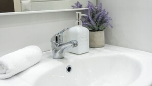 A bathroom sink with a chrome faucet, a white soap dispenser, and a rolled white towel. - Deluxe Double Room 101 (Catania)