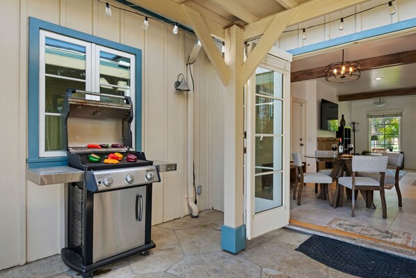 A kitchen with a grill, a dining area with chairs and a table, and a door leading to another room.