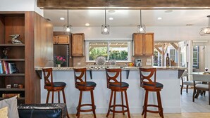 A kitchen with wooden cabinets, a central island with stools, pendant lighting, and a view to the outside. - NEW Steps to the Sand on Mesa Lane 3 BD 2BA with Jacuzzi! (Santa Barbara)