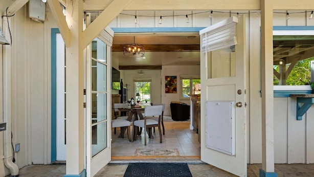 An open doorway leading to a dining area with a chandelier, a dining table with chairs, and a kitchen in the background. - NEW Steps to the Sand on Mesa Lane 3 BD 2BA with Jacuzzi! (Santa Barbara)