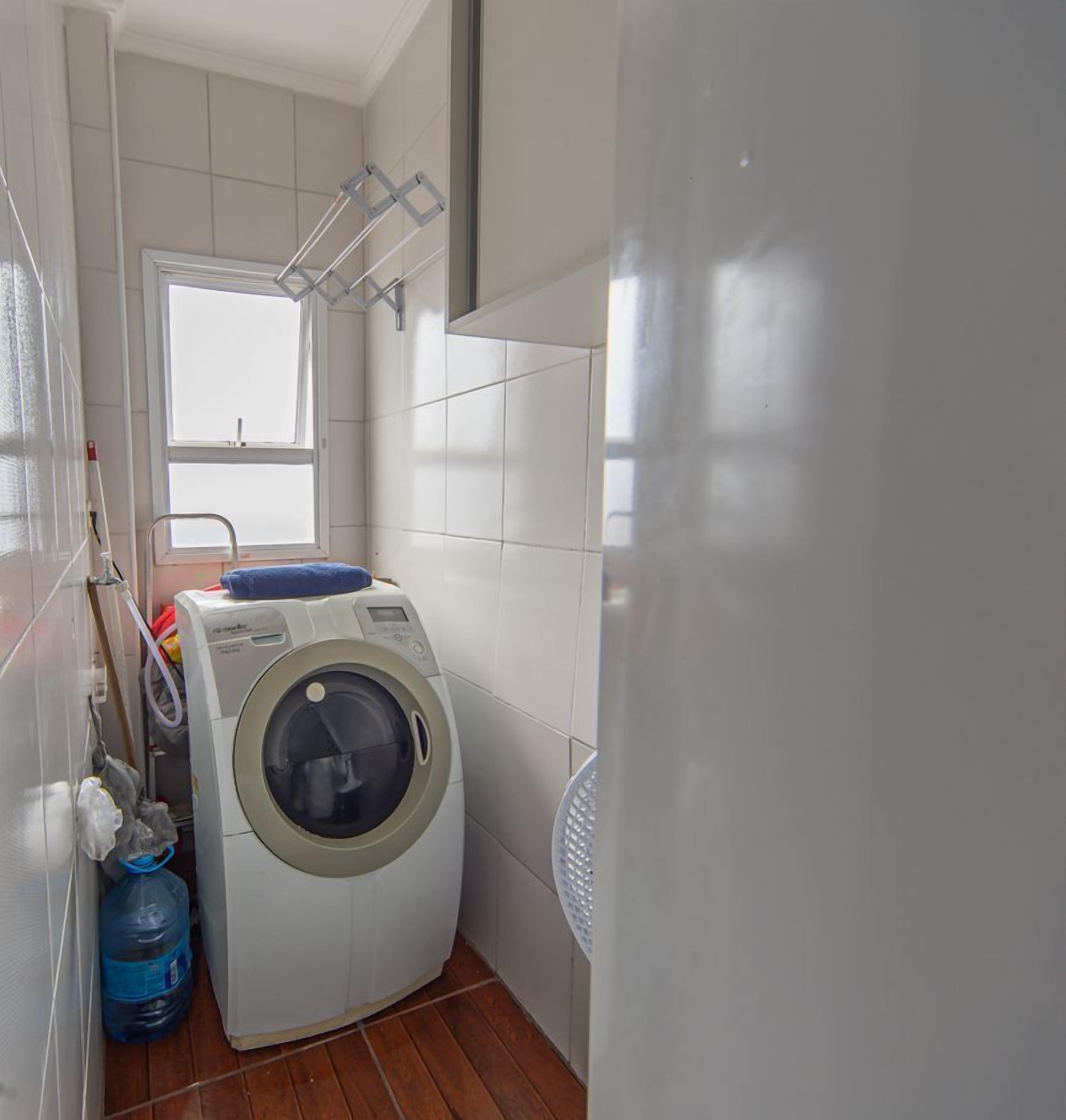 Een kleine wasruimte met een voorlader wasmachine, een droogrek en een grote waterreservoir.