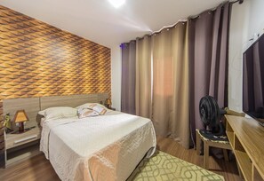 A hotel room with a bed, a desk, a chair, a fan, and a TV. - Apartamento Beira Mar com Varanda e Churrasqueira (Praia Grande)