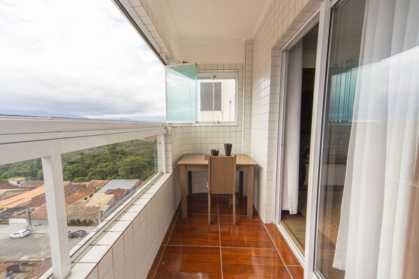 A balcony with a view of the city, a small table with chairs, and a window with a view. - Apartamento Beira Mar com Varanda e Churrasqueira (Praia Grande)