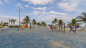Ein Strandspielplatz mit Schaukeln und Rutschen, Palmen und einem klaren Himmel.