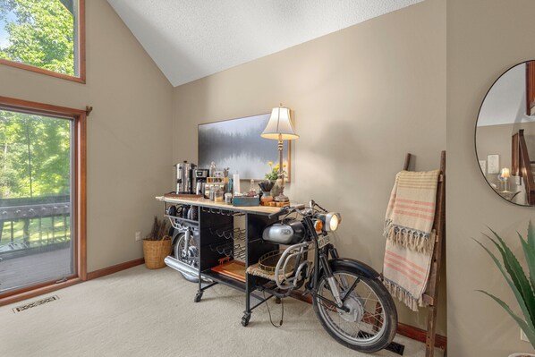 A room with a bicycle, a lamp, a mirror, and a window with a view of trees.