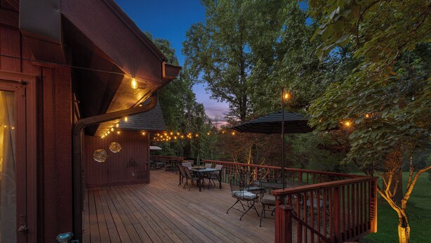Une terrasse en bois, dotée de meubles d’extérieur, de guirlandes lumineuses et offrant une vue sur les arbres.