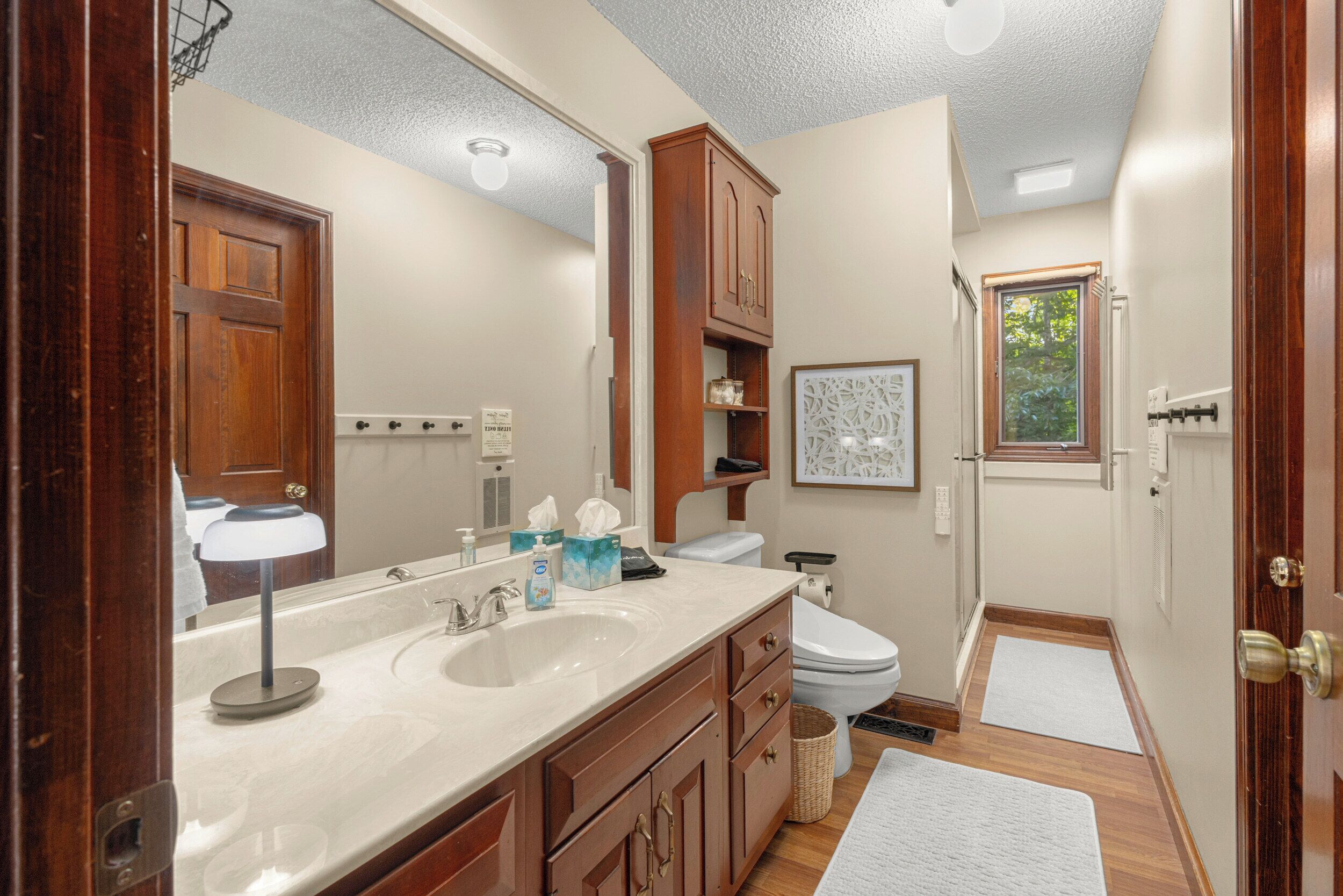 A bathroom with a double sink, wooden cabinets, a toilet, and a window.
