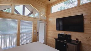 Habitación con paneles de madera, una cama, un televisor montado en la pared y una ventana con persianas.