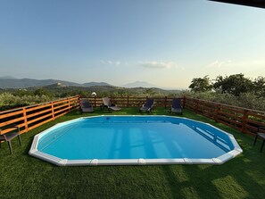 Piscina com deck de madeira e espreguiçadeiras, rodeada por uma cerca de madeira, com vista para montanhas ao longe.