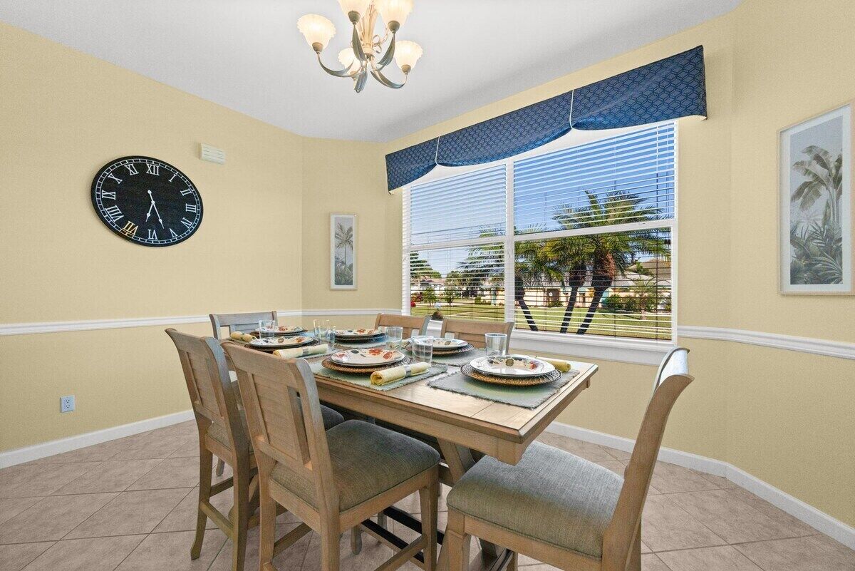 Un comedor con una mesa dispuesta para cuatro personas, un reloj de pared y una ventana con persianas.